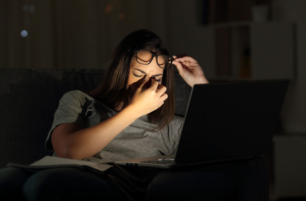 Woman frustrated due to dry eye when using laptop during night on sofa
