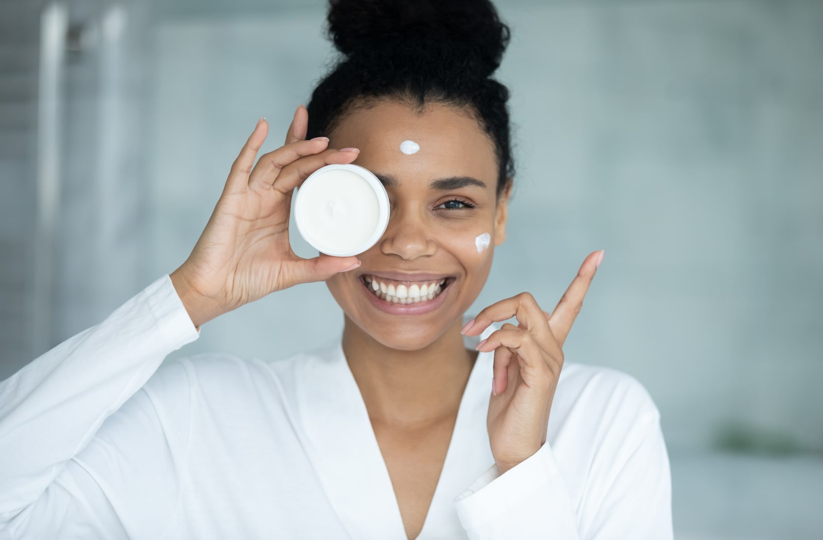 A woman smiling and putting face cream on her face